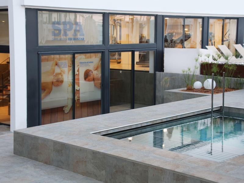 Área de piscina moderna con tumbonas frente a grandes ventanas de cristal de una zona de spa.