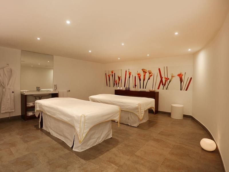 Habitación de spa moderna con dos camillas, iluminación suave y decoración minimalista.