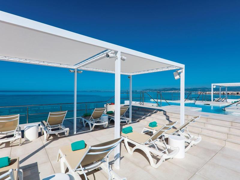 Moderna terraza en la azotea con tumbonas, toldos y vista al mar azul.