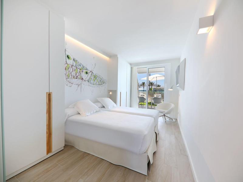 Habitación de hotel luminosa con cama doble, decoración blanca y balcón con vista exterior.