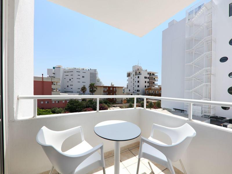 Balcón con dos sillas blancas y mesa redonda pequeña frente a edificios de la ciudad bajo cielo despejado.