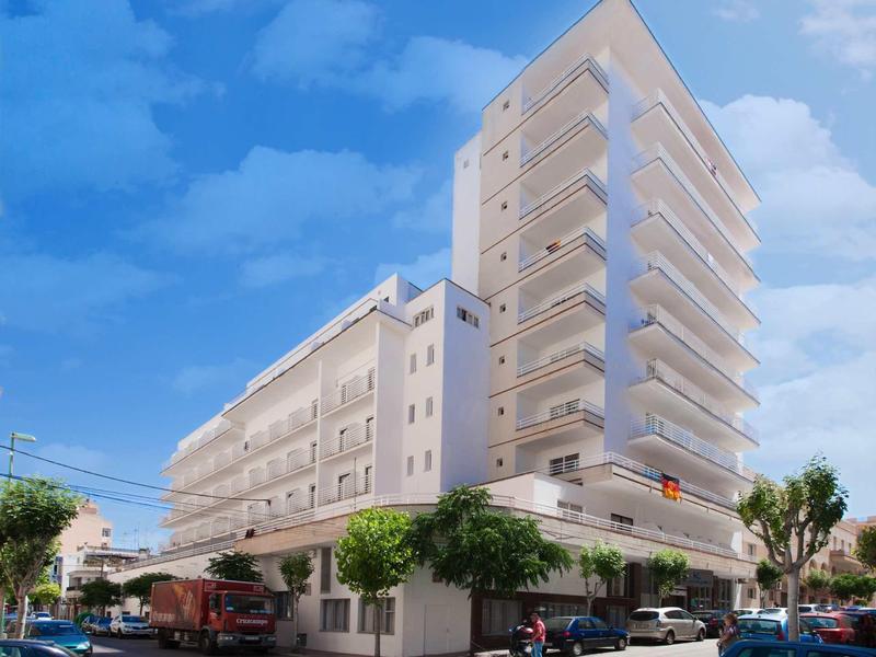 Moderní vícepatrová hotelová budova s balkony na rohu ulice pod modrou oblohou.