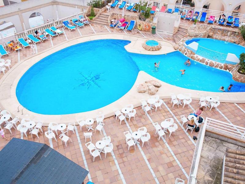 Velký venkovní bazén s lehátky a stoly kolem v hotelové oblasti.