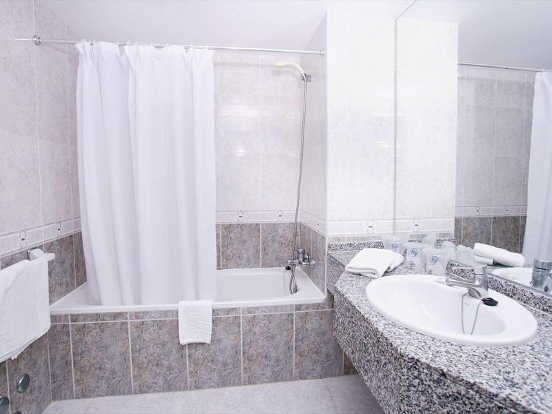 Světla koupelna s vanou, bílým závěsem do sprchy a granitovou umyvadlovou deskou se zrcadlem.