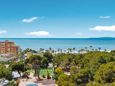 Vue d'une piscine d'hôtel avec des chaises longues, des palmiers et la mer bleue en arrière-plan.
