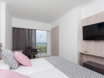 Chambre d'hôtel moderne avec lit double, télévision écran plat et balcon avec vue sur la mer.