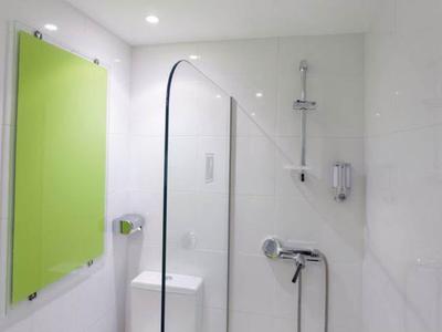 Douche lumineuse avec cloison en verre, panneau mural vert et accessoires modernes.