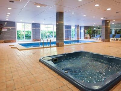 Espace piscine intérieure avec jacuzzi et grandes fenêtres laissant entrer la lumière naturelle.