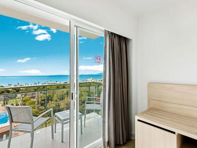 Habitación de hotel con balcón, vistas al mar, jardín, diseño interior moderno y ambiente luminoso