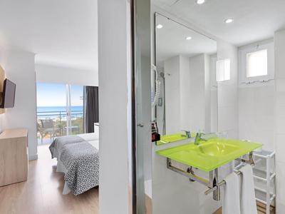 Chambre d'hôtel moderne avec vue sur la mer, sol en bois clair et salle de bain adjacente avec lavabo vert.