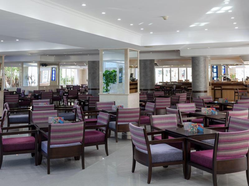 Grande salle à manger lumineuse avec plusieurs tables et chaises rayées roses dans un hôtel.