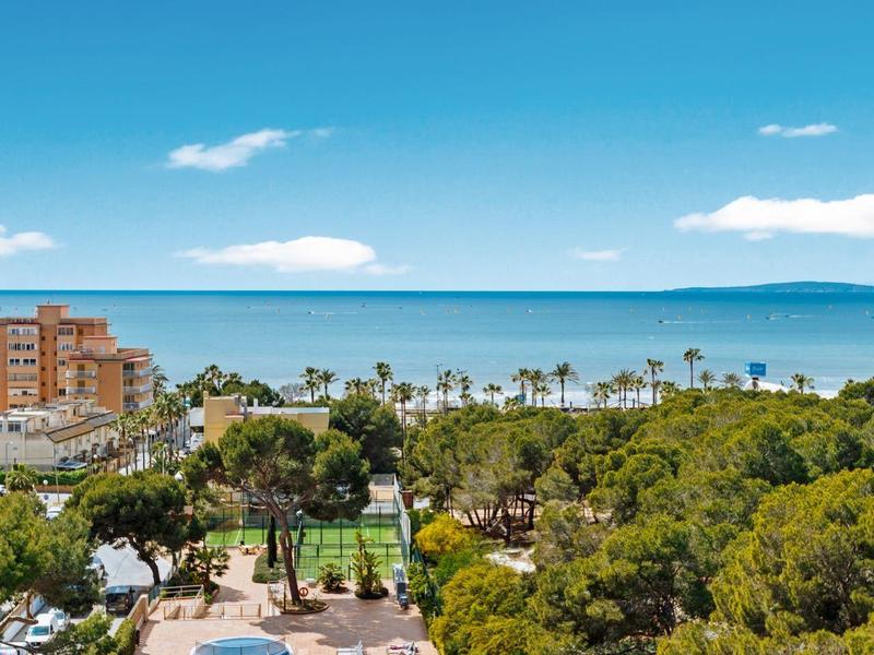 Vue d'une piscine d'hôtel avec des chaises longues, des palmiers et la mer bleue en arrière-plan.