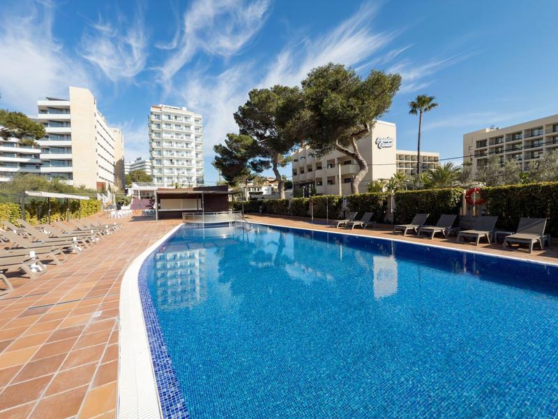Grande piscine avec transats dans une station balnéaire sous un ciel bleu.