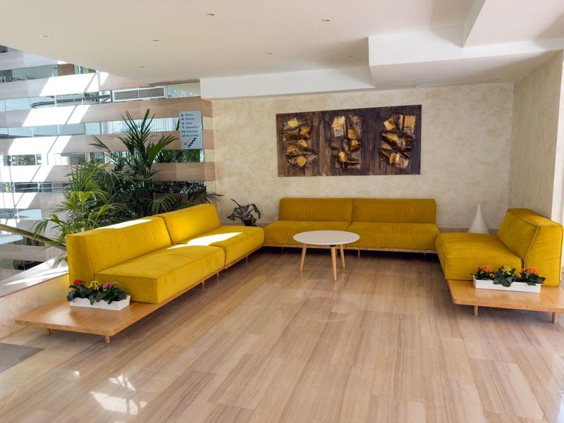 Salon moderne avec canapés jaunes, sol en bois et décorations murales de feuilles.