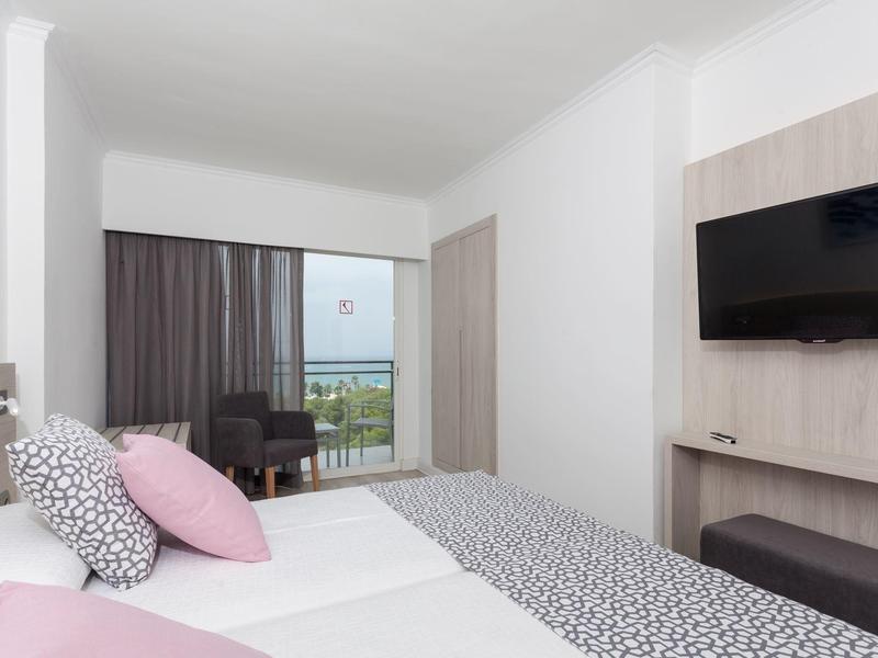 Chambre d'hôtel moderne avec lit double, télévision écran plat et balcon avec vue sur la mer.