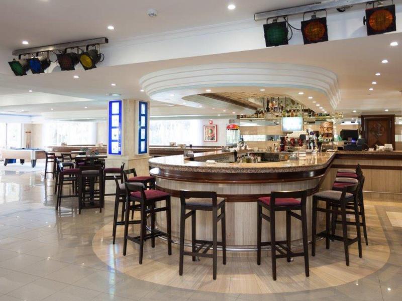 Espace bar d'hôtel lumineux avec des chaises modernes et un comptoir rond sous des luminaires encastrés.