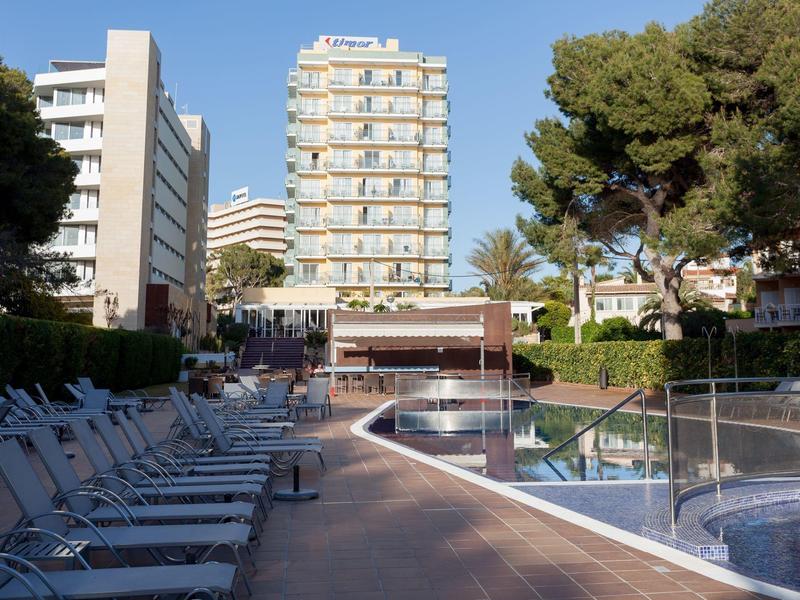 Zone de piscine vide avec chaises longues et bâtiments d'hôtel en arrière-plan par une journée ensoleillée.