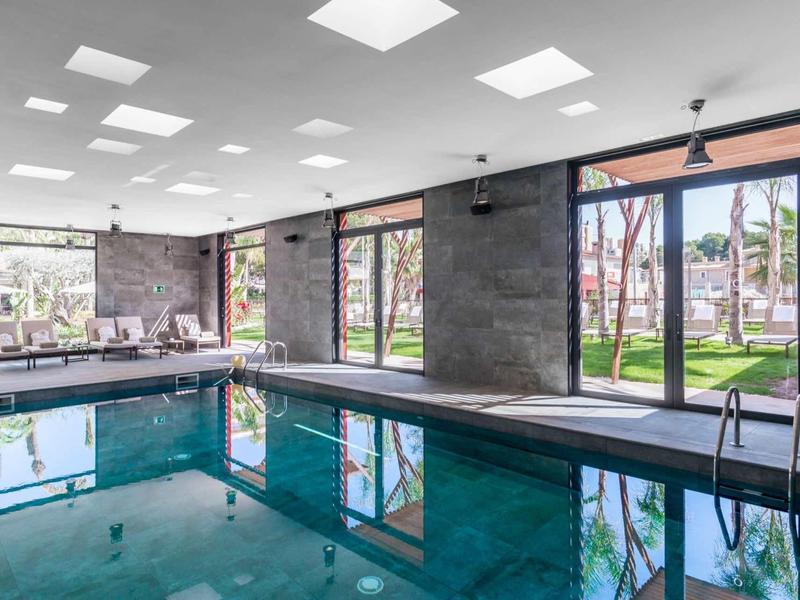 Basen kryty z dużymi oknami, widokiem na ogród i nowoczesnym minimalistycznym wystrojem.