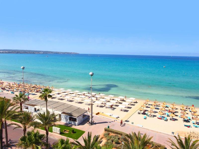 Plaża z parasolami, palmami i czystym niebieskim morzem w słoneczny dzień.