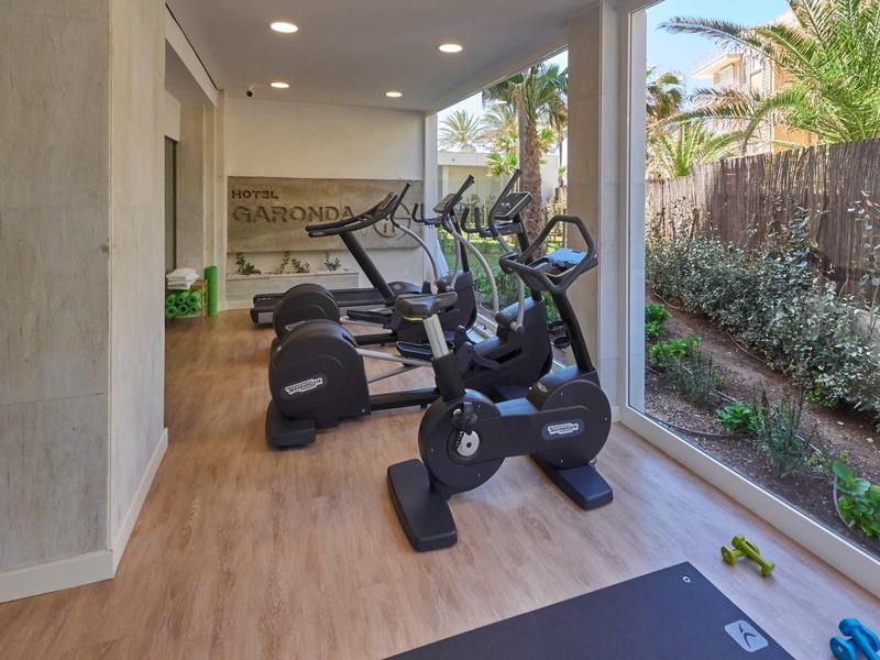 Nowoczesna siłownia z bieżniami i stepperami obok dużych okien z widokiem na ogród.