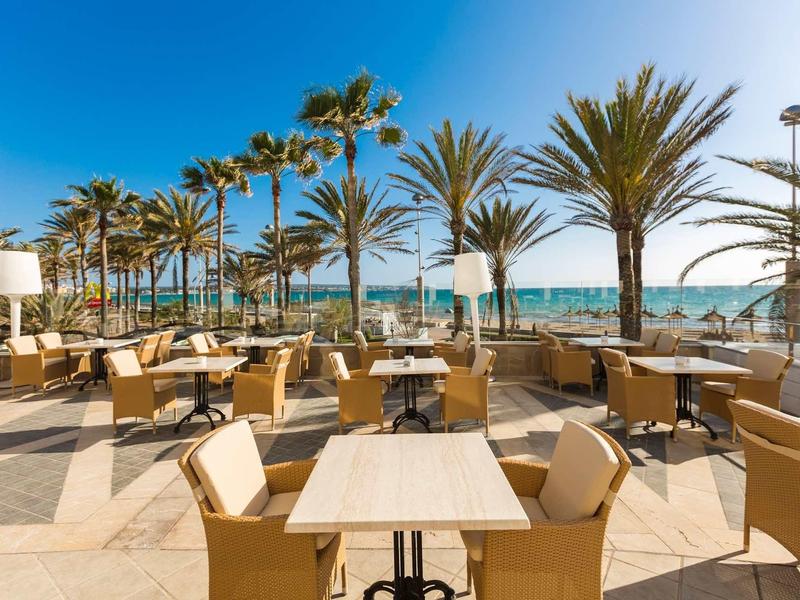 Taras na plaży z krzesłami i stołami pod palmami w słoneczny dzień.