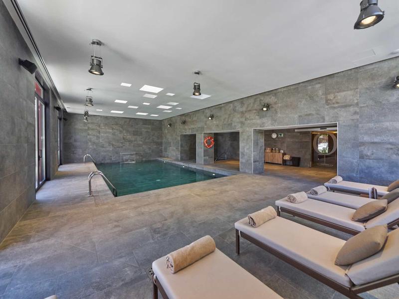 Nowoczesny basen kryty z leżakami w betonowym pomieszczeniu z dużymi oknami