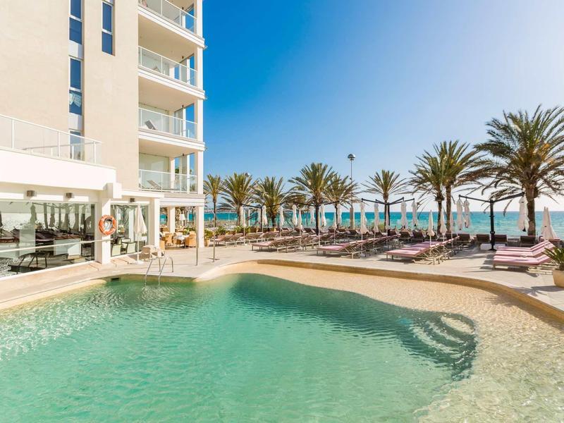 Basen hotelowy z leżakami i palmami pod czystym błękitnym niebem nad morzem