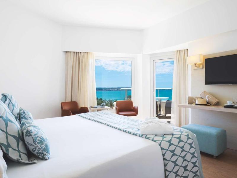 Jasny pokój hotelowy z dużym łóżkiem, balkonem i widokiem na morze