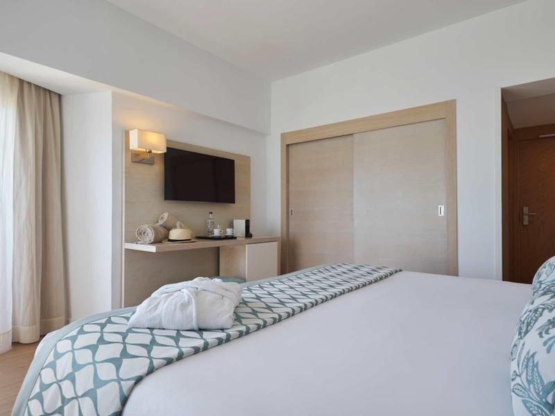 Jasny pokój hotelowy z dużym łóżkiem, telewizorem z płaskim ekranem i oknem z zasłonami.