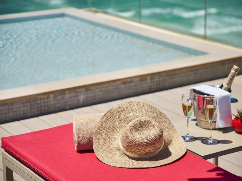 Taras przy basenie z czerwonym leżakiem, słomkowym kapeluszem, ręcznikiem i szampanem z kieliszkami.