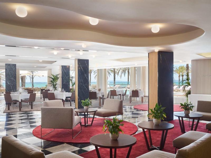 Nowoczesna przestrzeń lobby hotelowego z miejscami do siedzenia, czerwonymi dywanami i widokiem na tropikalne palmy.