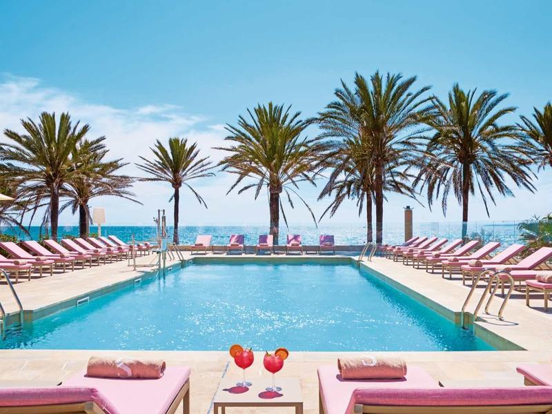 Obszar basenu z leżakami przy palmach i widokiem na morze przy czystym niebie.