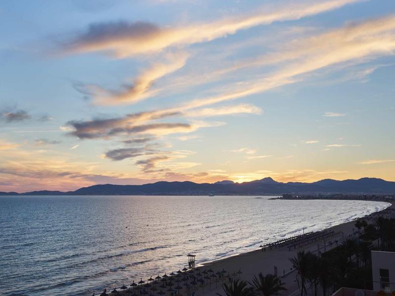 Widok na plażę z spokojnym morzem i kolorowym niebem o zachodzie słońca.
