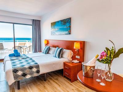 Habitación de hotel moderna con vistas al mar, cama doble y balcón con sillas.