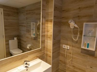 Modernes Badezimmer mit Holzoptik-Fliesen, großem Spiegel, Waschbecken, Toilette und Haartrockner.
