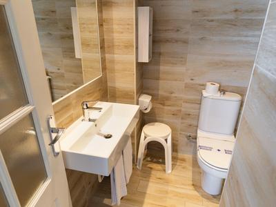 Kleines modernes Badezimmer mit weißem Waschbecken, WC, Holzoptik-Fliesen und einem kleinen Hocker.
