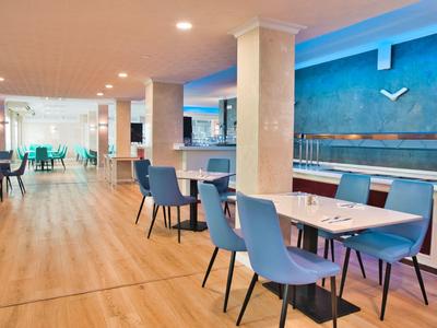 Moderner Speisesaal mit blauen Stühlen, weißen Tischen und hellbraunem Holzboden.