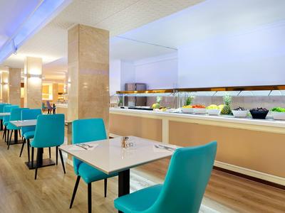 Moderner Speisesaal mit blauen Stühlen, weißen Tischen und Buffetbereich mit vielfältigen Speisen.