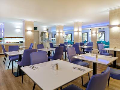 Modernes Restaurant mit hellen Tischen, lila Stühlen und sanfter Beleuchtung.
