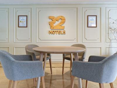 Moderner Sitzbereich mit rundem Holztisch, vier grauen Sesseln und heller Wand mit Deko und Logo.