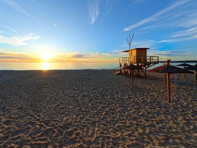 Strand bei Sonnenuntergang mit Holzrettungsturm, Sand und blau-orangefarbenem Himmel.