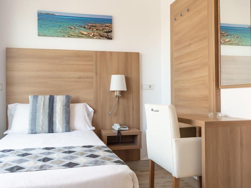 Cozy hotel room with a single bed, wooden furniture, a white chair, and ocean artwork.