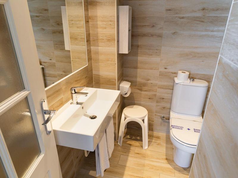 Modern bathroom with wood-look tiles, white sink, toilet, and small white stool.