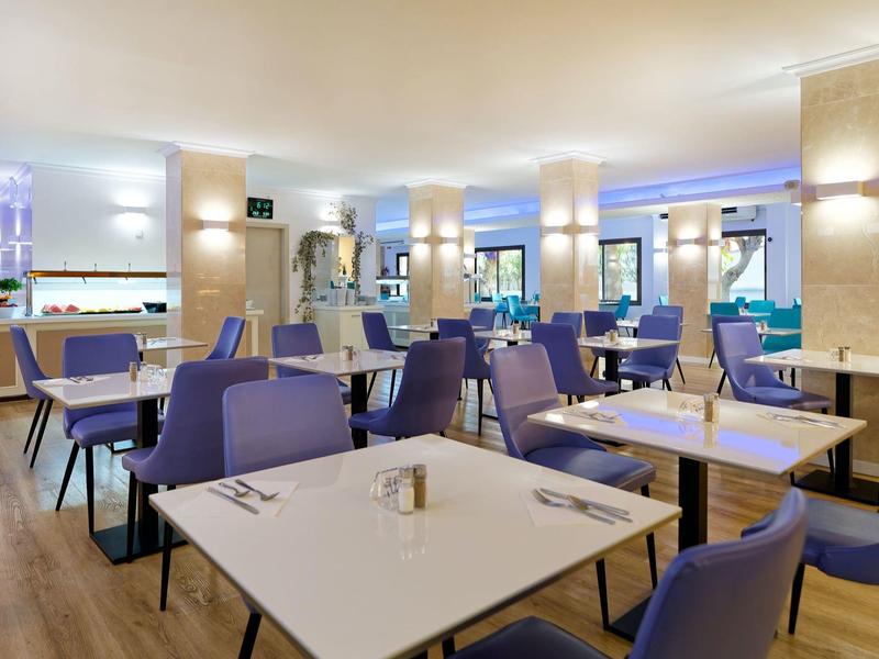 Modern hotel dining area with white tables, purple chairs, and soft ambient lighting.