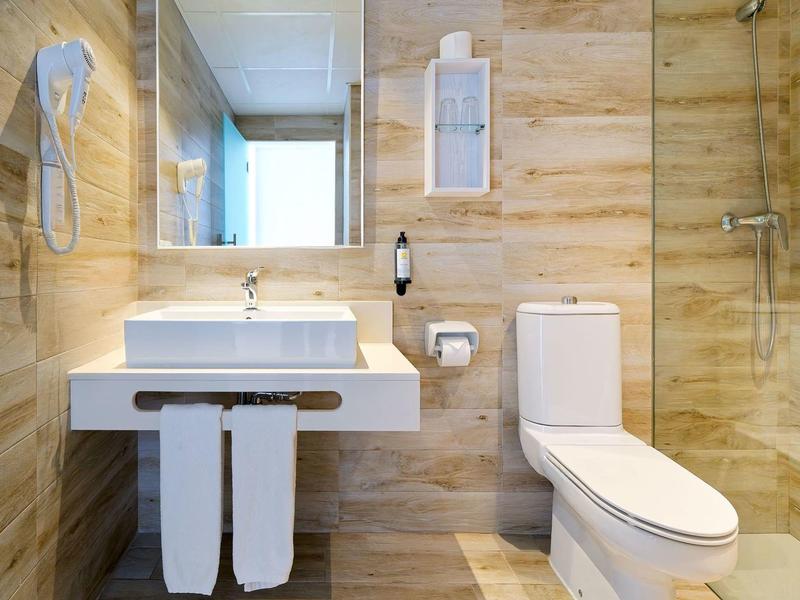 Modern hotel bathroom with beige marble walls, white sink, mirror, hairdryer, and toilet.