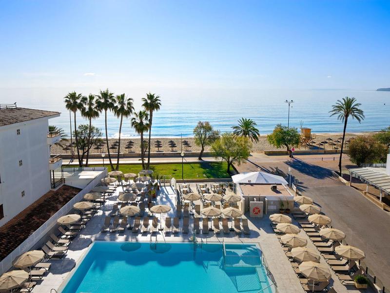 Resort pool area with sun loungers and umbrellas by the sea under a clear sky.