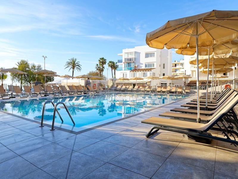 Sunny outdoor pool area with lounge chairs and umbrellas next to a hotel building.
