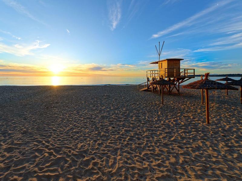 Sunset over an empty sandy beach with a lifeguard tower and shaded benches.