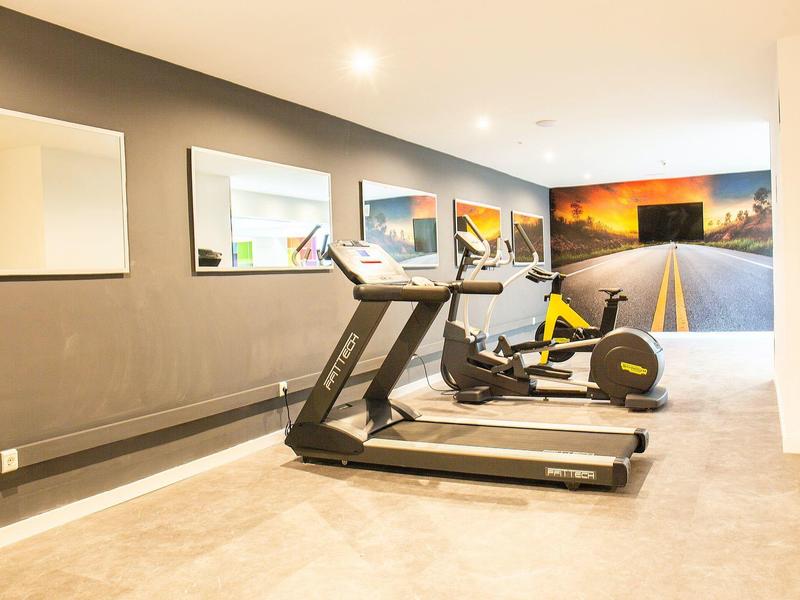 Gimnasio moderno con cinta de correr y bicicleta estática frente a una pared con mural de carretera.