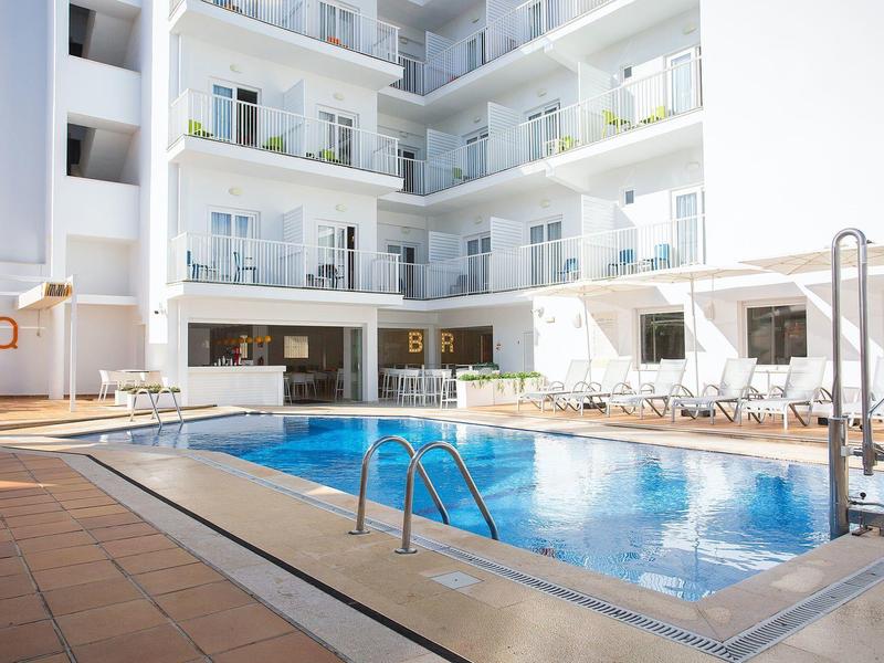Piscina moderna de hotel con tumbonas y balcones en un edificio blanco.